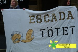 Foto, zwei Personen halten Banner mit der Aufschrift "Escada tötet"